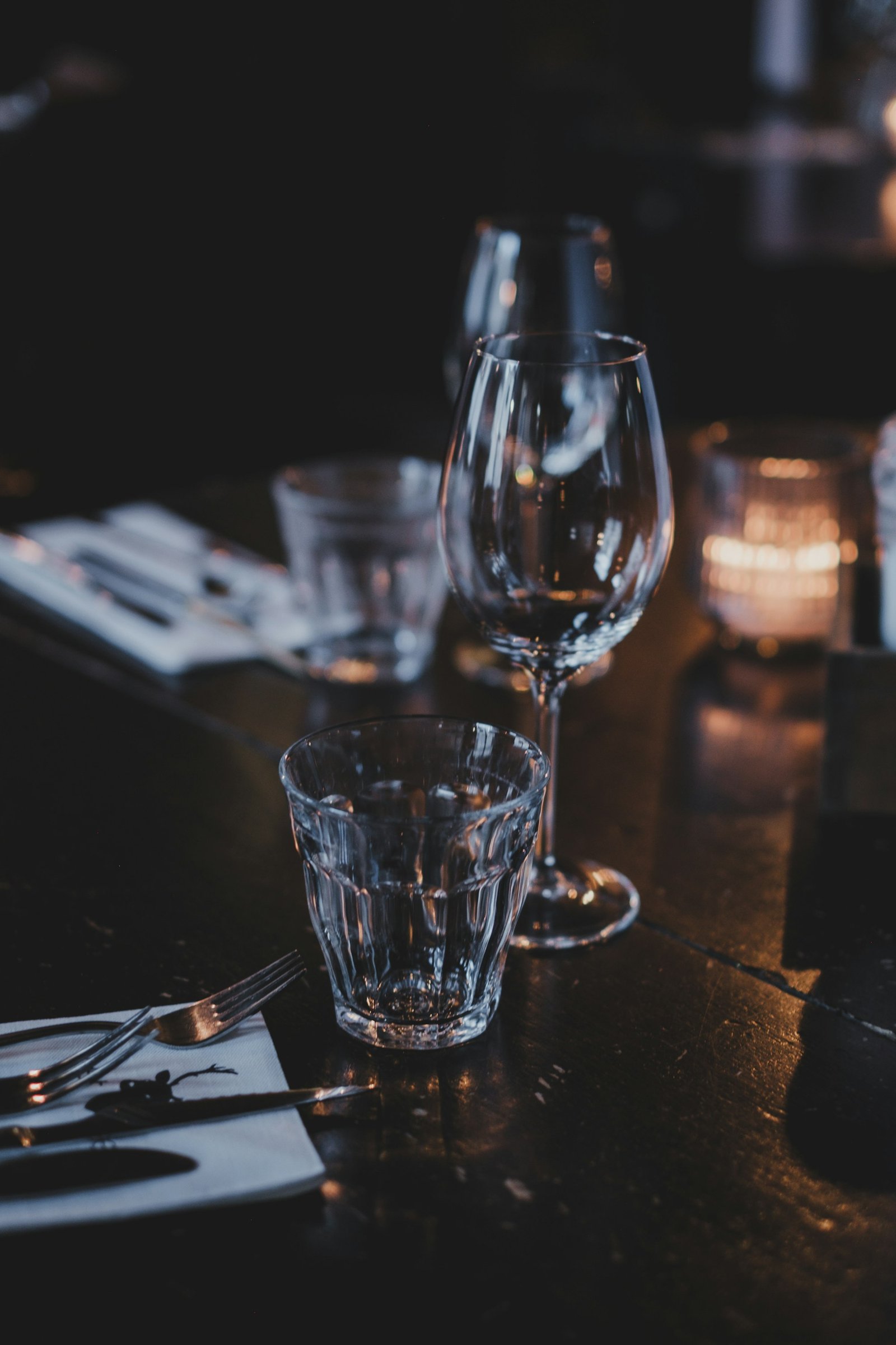 Verres et couverts disposés sur une table sombre.